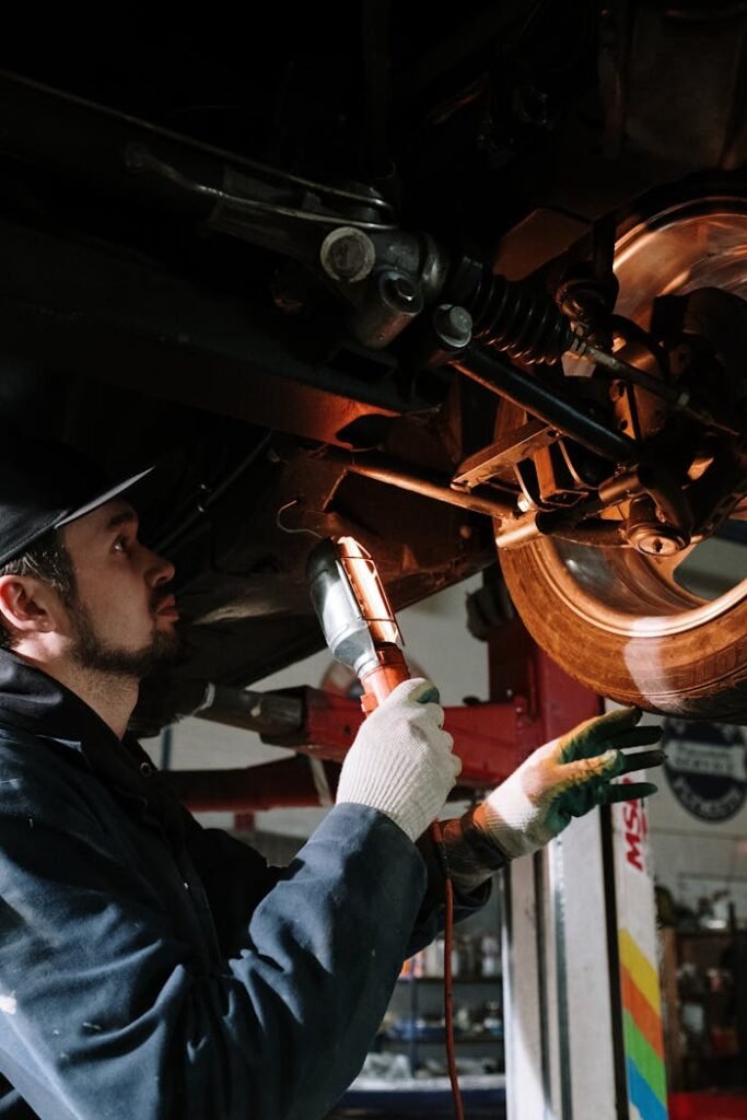 man-in-blue-dress-shirt-holding-brown-wooden-tool-4489737 Mechanic uses a flashlight to inspect cars suspension in a garage setting.